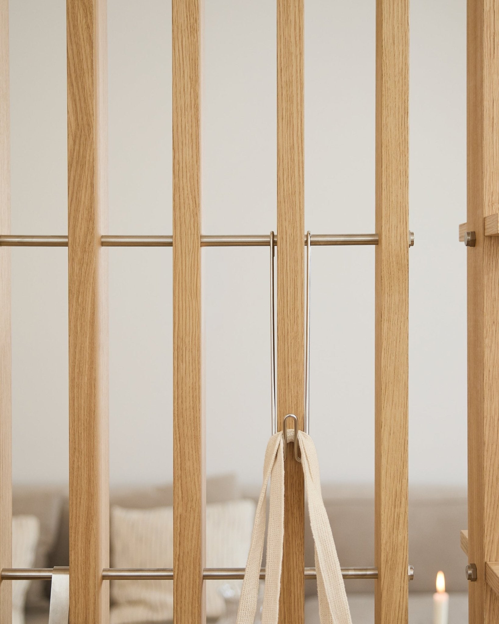 Ljus träport med metallstänger, beige snöre och tre WoodUpp Alva Wire Hooks/BM1; en suddig soffa och ett ljus i bakgrunden.